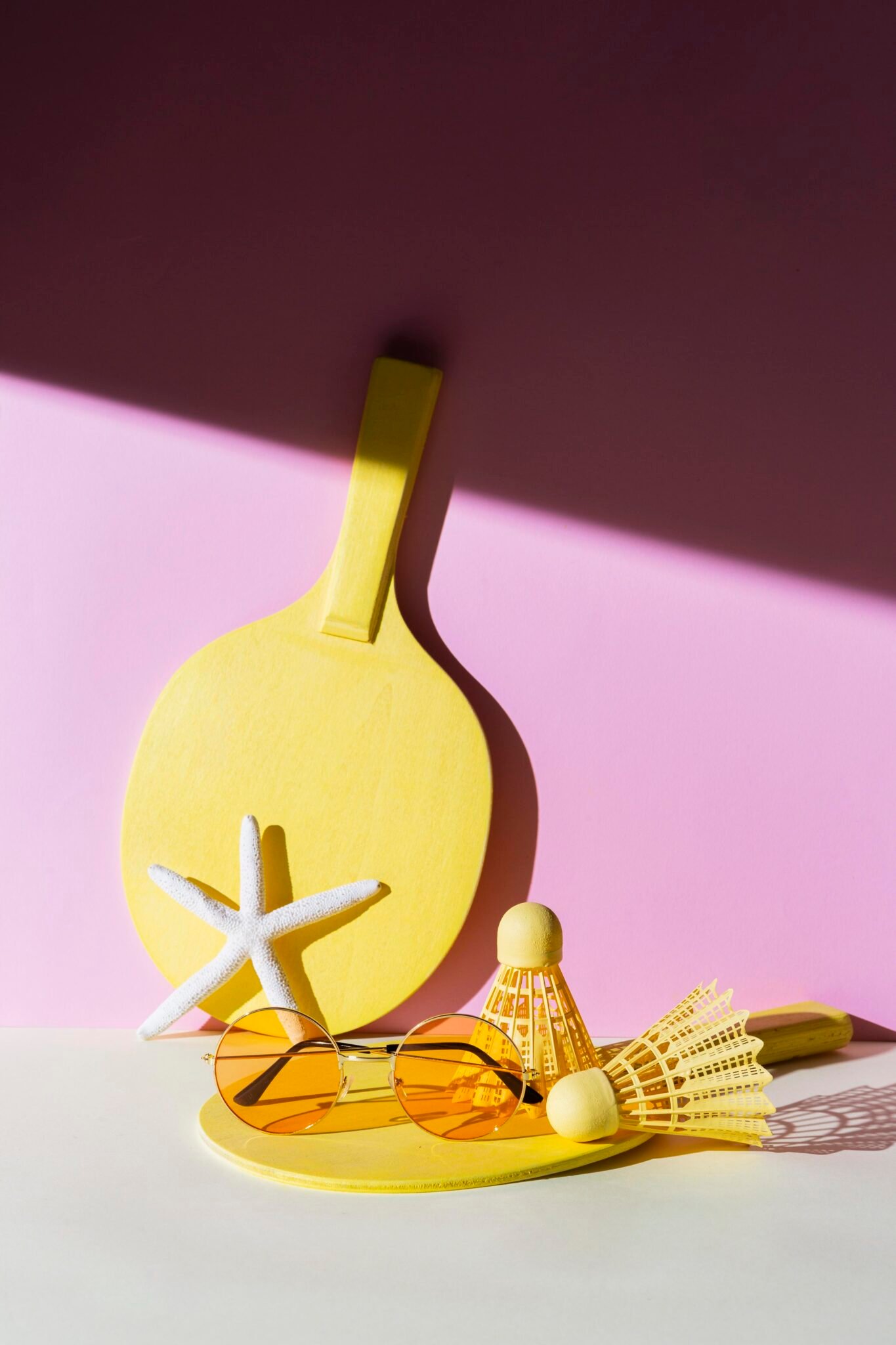 Accesorios deportivos de playa en tonos amarillos sobre fondo rosa y blanco.
